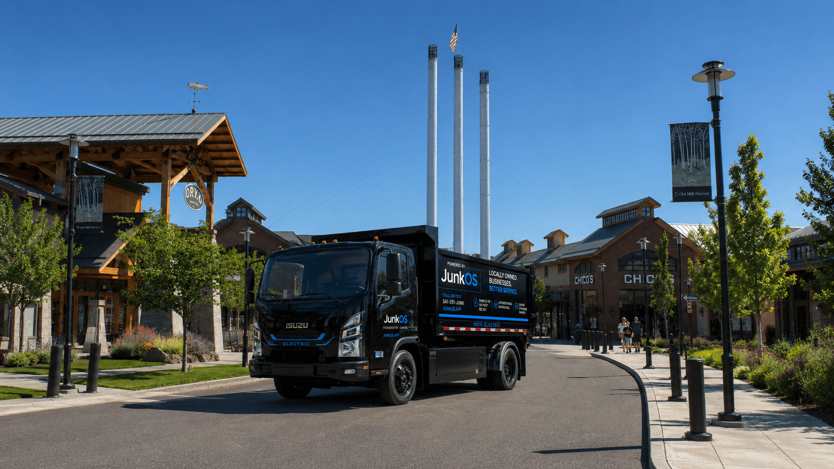 JunkOS black electric dump truck parked in Bend's Old Mill District under a clear blue sky.